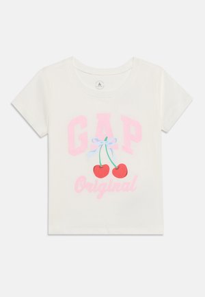 T-shirt blanc à manches courtes avec le texte rose "GAP Original" et deux cerises rouges aux tiges vertes attachées par un nœud bleu au centre.