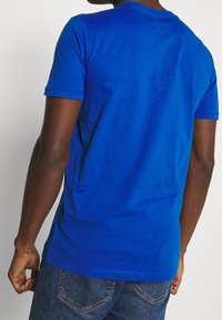 Kurze ärmelschutz in blau aus Baumwolle mit rundem Halsausschnitt, glatter Textur und tailliertem Schnitt, von hinten gezeigt.