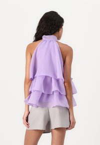 Lilla lagdelt topp laget av lett stoff med volanger. Halterneck-design, åpen rygg, kombinert med lysegrå shorts.