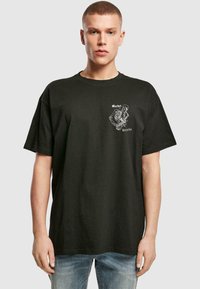 Must musta T-särk lühikeste varrukatega, vabalt lõigatud, millel on vasakul rinnal valge skeletoni graafika ja tekst. Lihtne disain.