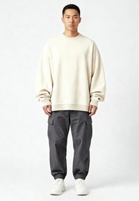 Lichtbeige oversized sweatshirt met geribbelde manchetten, gecombineerd met donkergrijze cargobroek met zijzakken en elastische manchetten. Witte sneakers maken de look af.