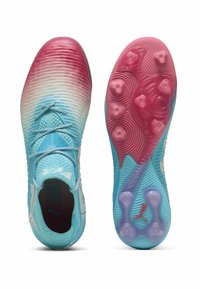 Jasnoniebieskie i różowe korki piłkarskie posiadają gradientowy wzór, żebrowaną fakturę, wyraźne sznurowadła oraz wzorzystą podeszwę z stożkowymi kołkami.