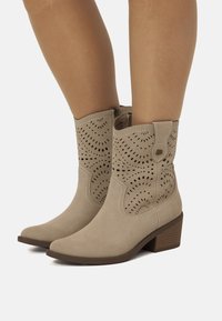 Botas de tobillo de ante beige con detalles troquelados, punta afilada y un pequeño tacón. Cierre lateral para ponerlas y quitarlas fácilmente.