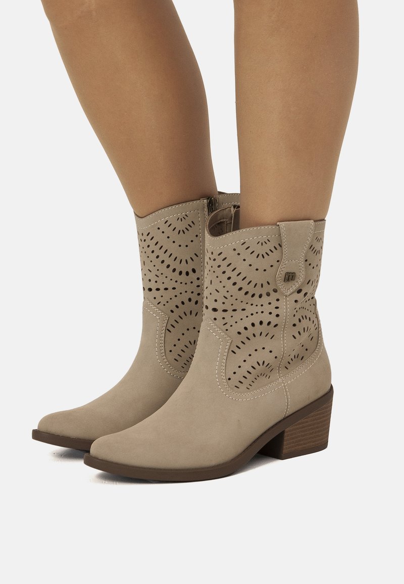 Botas de tobillo de ante beige con detalles troquelados, punta afilada y un pequeño tacón. Cierre lateral para ponerlas y quitarlas fácilmente.