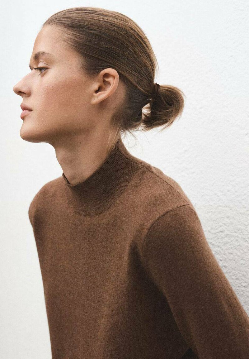 Brauner Wollrollkragenpullover mit figurbetontem Schnitt, glatter Textur und minimalen Nähten. Modell im Profil mit einfacher Frisur gezeigt.