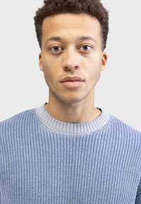 Light blue knitted sweater with ribbed texture and round neckline, featuring vertical stripes and a soft, lightweight fabric.