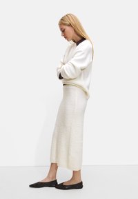 Biały sweter o fakturze i dopasowana spódnica, w połączeniu z ciemnobrązowymi balerinami, tworzą minimalistyczny look. Prosta sylwetka z miękkich materiałów.