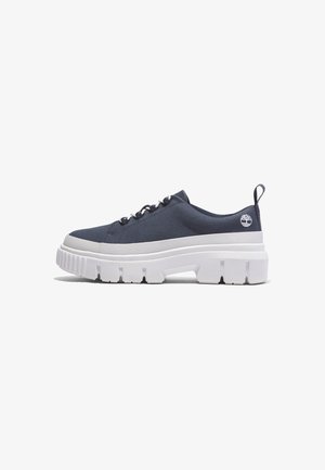 Baskets basses bleu marine avec une semelle épaisse blanche et volumineuse, fermeture à lacets, languette au talon et un petit logo d'arbre près du talon.