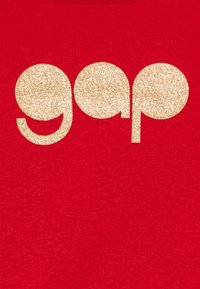 T-shirt rossa con grande logo dorato "gap" glitterato. Maniche corte, scollatura rotonda, tessuto morbido.
