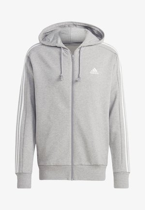 Felpa grigia con chiusura a zip realizzata in tessuto morbido, dotata di cappuccio, tasche frontali e dettagli a tre strisce bianche lungo le maniche. Logo Adidas sul petto.