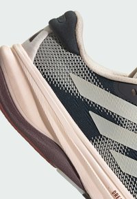 Scarpa da corsa con una tomaia in rete nera traspirante, dettagli grigi e una suola texturizzata rosa e viola. Caratterizzata da un design aerodinamico e strisce distintive.