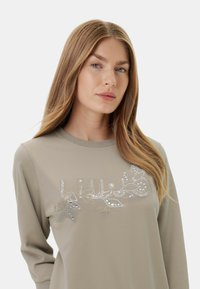 Felpa beige chiaro a maniche lunghe con un design floreale decorativo in strass sul petto. Tessuto morbido con scollatura rotonda.