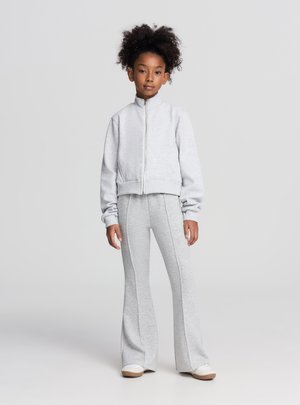 Felpa grigia con zip abbinata a pantaloni della tuta grigi a campana, entrambi realizzati in tessuto morbido. Presentano polsini a coste e cuciture laterali sui pantaloni.