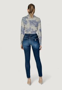 Bloemengestikt shirt met lange mouwen, in blauw en beige kleuren, gecombineerd met strakke donkerblauwe jeans, met hoge taille en subtiele achterzakken.