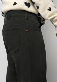 Olivgrüne Hose mit schmaler Passform, aus robustem Gewebe. Verfügt über zwei Gesäßtaschen und kontrastierende Kupferdetails.