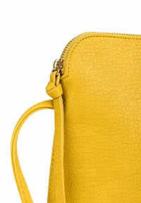 Žlutá kožená kabelka s texturovaným povrchem a horním zipem. Má uzlový popruh a detaily ve zlaté barvě.