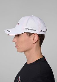 Biała czapka z zakrzywionym daszkiem, z czarnym logo Pumy, brandingiem TAG Heuer i Ansys po bokach. Materiał wydaje się teksturowany.