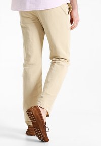 Hnědé, texturované boty s unikátním tečkovaným detailem na podrážce. Nosené s jasně béžovými slim-fit kalhotami, které podtrhují design a barevný kontrast bot.