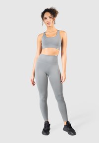 Szary, sportowy stanik treningowy oraz legginsy z wysokim stanem, wykonane z elastycznego, gładkiego materiału; stylizowane z minimalną liczbą szwów i czarnymi butami sportowymi.