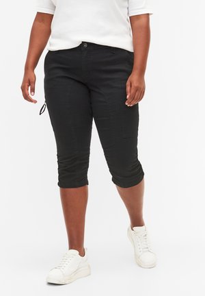 Pantaloni neri cropped realizzati in un tessuto misto cotone, con una vestibilità slim, risvolti e tasche laterali. Abbinati a sneakers bianche.