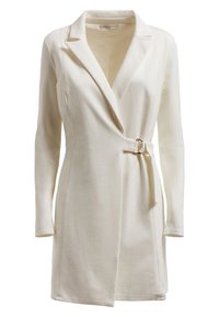 Robe blazer couleur crème avec manches longues, col cranté, ceinture frontale avec boucle argentée, et tissu lisse et texturé.