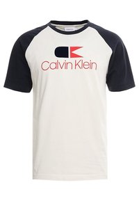 Camiseta de manga corta con cuerpo color crema y mangas raglán en azul marino. Presenta un logo de Calvin Klein en rojo y azul marino en el frente. Material de algodón.