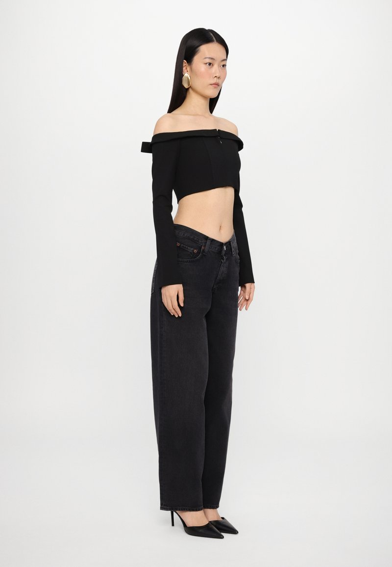 Crop top noir décolleté avec manches longues, associé à un jean en denim noir taille haute et des escarpins noirs à bout pointu.