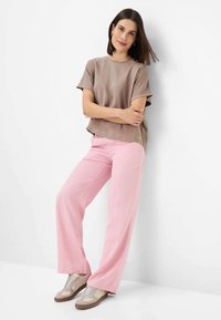 Bruine korte mouw top, roze wijde broek en lichtgekleurde sneakers; gladde textuur met minimale accenten en een casual pasvorm.