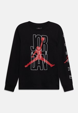 Chemise noire à manches longues avec une grande silhouette rouge de joueur de basket dunkant, surmontée d’un texte blanc contouré « JORDAN » à l’avant.