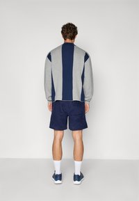 Grå og marineblå fargeblokkert hettegenser med ribbestrikkede mansjetter, parret med marineblå kordfløyelsshorts. Hvite sporty sokker og mørke joggesko fullfører antrekket.