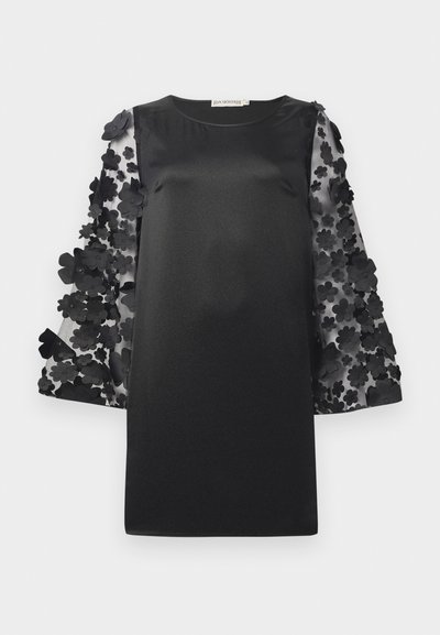 Must must, millekoolse kehajoonise ja läbipaistvate varrukatega, mis on kaunistatud kihiliste lilleaplikatsioonidega. Ümar kaelus ja lõdva soe sobivus.