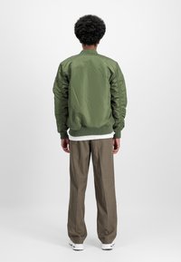 Olive green bomber jacket with ribbed cuffs and collar, paired with beige trousers and white sneakers, viewed from the back.