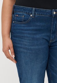 Tumed sinised teksad sileda tekstuuriga. Omavad eesmist taskut, metallist nööpi ja õmblustoodet vöökohal.