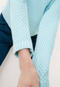Pull tricoté bleu clair avec un motif texturé. Poignets côtelés aux manches. Le tissu semble doux et confortable.