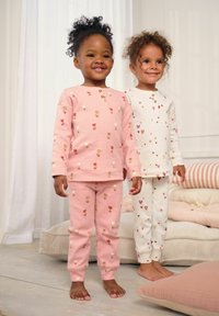 To børn har matchende pyjamasæt på: den ene i pink med blomster mønster, og den anden i hvid med hjerte design. Begge har lange ærmer og bukser.