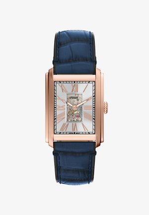 Fossil rechteckige Uhr mit einem roségoldfarbenen Gehäuse, weißem Ziffernblatt, blauen Lederarmband und einem skelettierten Uhrwerk, das die inneren Mechanismen zeigt.