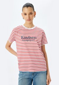 Rød og hvidstribet t-shirt med rund hals og korte ærmer. Har teksten "Venlighed er en superkraft" i mørkeblå.