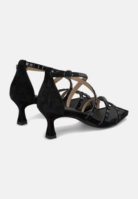 Schwarze Wildlederschuhe mit Absatz und quadratischer Zehenform, versehen mit gekreuzten Riemen und einer Metallschnalle, akzentuiert durch glänzende Details auf den Riemen.