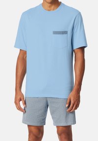 Himmelblaues Baumwoll-T-Shirt mit kurzen Ärmeln und einer Brusttasche, die mit einem schwarz-weißen Karomuster verziert ist, kombiniert mit passenden karomusternden Shorts.
