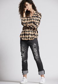 Schwarz-weiß gemusterte Bluse mit langen Ärmeln, kombiniert mit ausgefransten dunklen Jeans und weißen Sneakers. Bemerkenswerte Details sind die hochgerollten Säume.