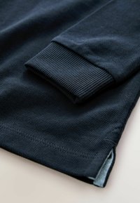 Mörkblå långärmad skjorta med ribbade manschetter, gjord av ett texturerat tyg och med sidofickor för passform och rörelse.