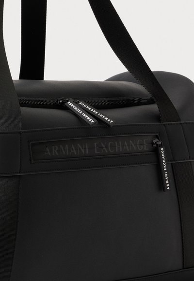 Крупен план на черна чанта Armani Exchange с широки презрамки, два горни ципа и преден джоб с цип.