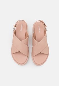 Sandales rose pâle avec des brides croisées, une boucle ajustable à la cheville et une semelle plate. Fabriquées en matériau synthétique lisse avec des coutures minimales.