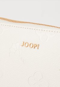 Biały skórzany woreczek z fakturowanej skóry z wypukłymi wzorami kwiatowymi, z logo w złotym kolorze "JOOP!" i złotym zamkiem błyskawicznym na górze.