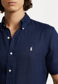 Navy blue short-sleeve shirt made of lightweight fabric, featuring a button-down collar and a white embroidered logo on the chest.
