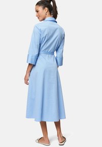 Helles blau gestreiftes Kleid mit einem Kragen, Dreiviertelärmeln und einem Taillengürtel. Der Stoff wirkt glatt, mit einem ausgestellt Rock bis zur Wadenlänge.