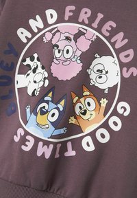 Sudadera morada con un gráfico circular que presenta animales de dibujos animados: un perro azul, un perro naranja, un caniche rosa, un perro negro moteado y una nube blanca.