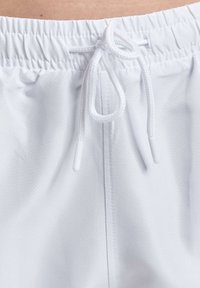 Hvite treningsshorts med teksturert stoff, elastisk livlinning og snorjustering. Designet har minimalistische stil.