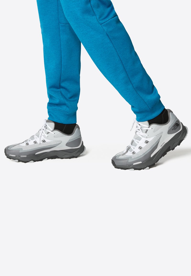 Graue und weiße Sportschuhe mit einem strukturierten Mesh-Obermaterial, verstärktem Fersenbereich und schwarzen Akzenten. Dicke Gummisohle für besseren Grip.