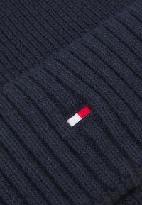 Beanie en tricot marine avec texture côtelée, présentant une petite étiquette logo rouge, blanche et bleue cousue sur le côté. Matériau durable en mélange de laine.